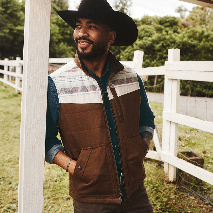 Man leaning against post in vest and cowboy hat